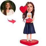 Das schöne Mädchen, das eine Geschenkbox hält, und Liebes-Herz-kundenspezifische Bobbleheads addieren Text